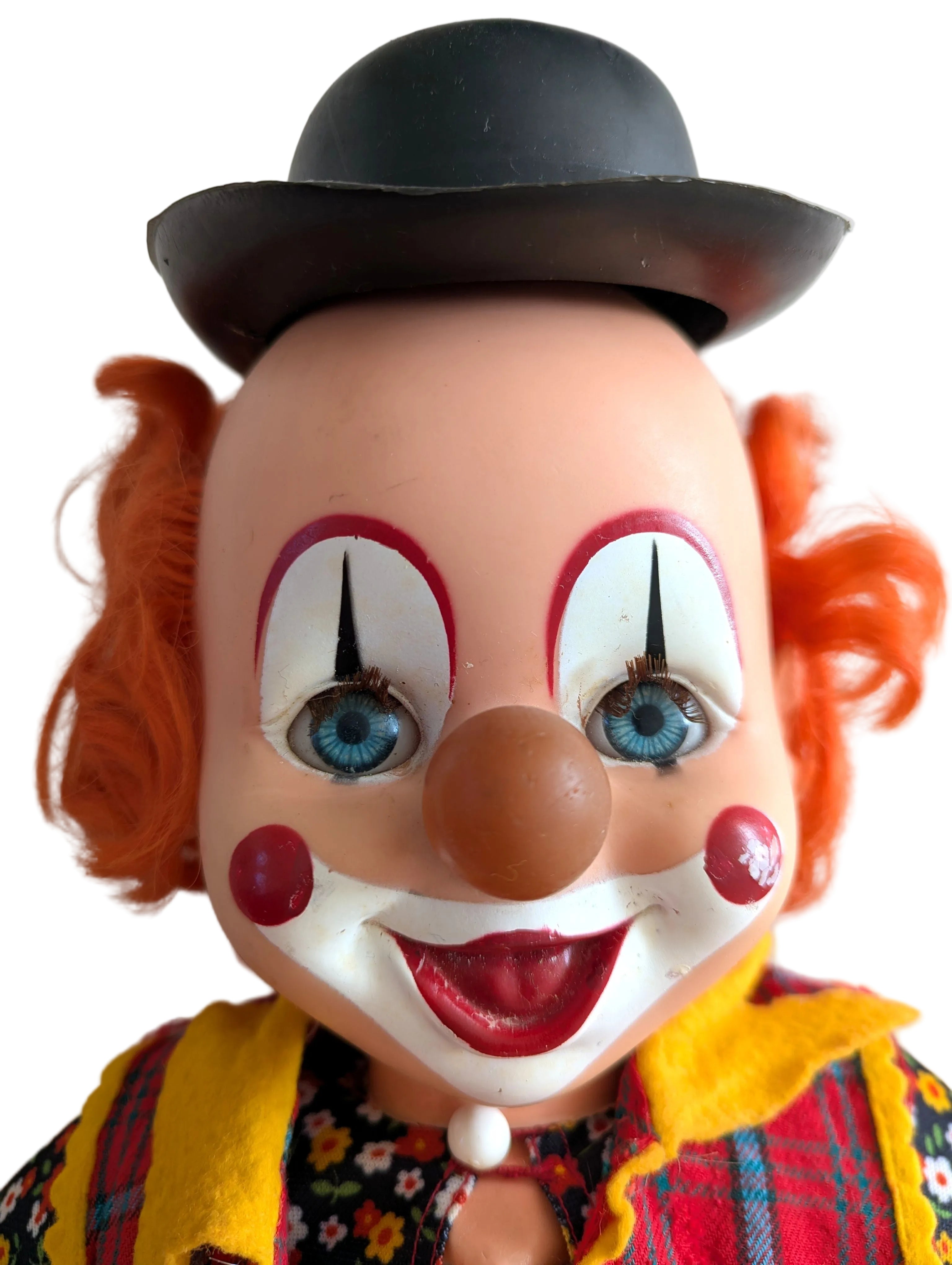 Vintage clown doll with orange hair, a black bowler hat, and a colorful plaid jacket against a plain light background.