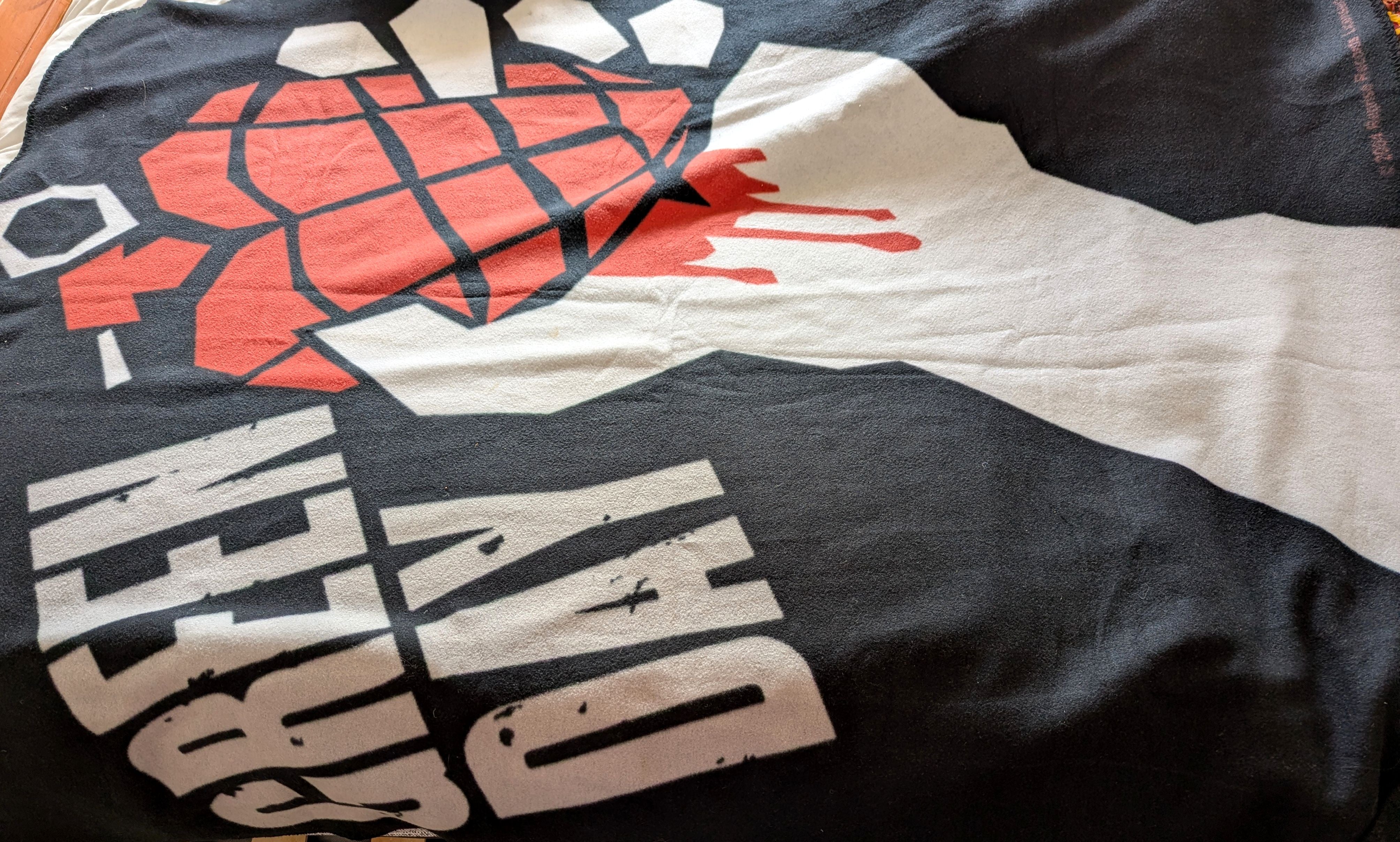 A close-up of a black blanket featuring the iconic Green Day 'Grenade' graphic with a red hand grenade and white text.