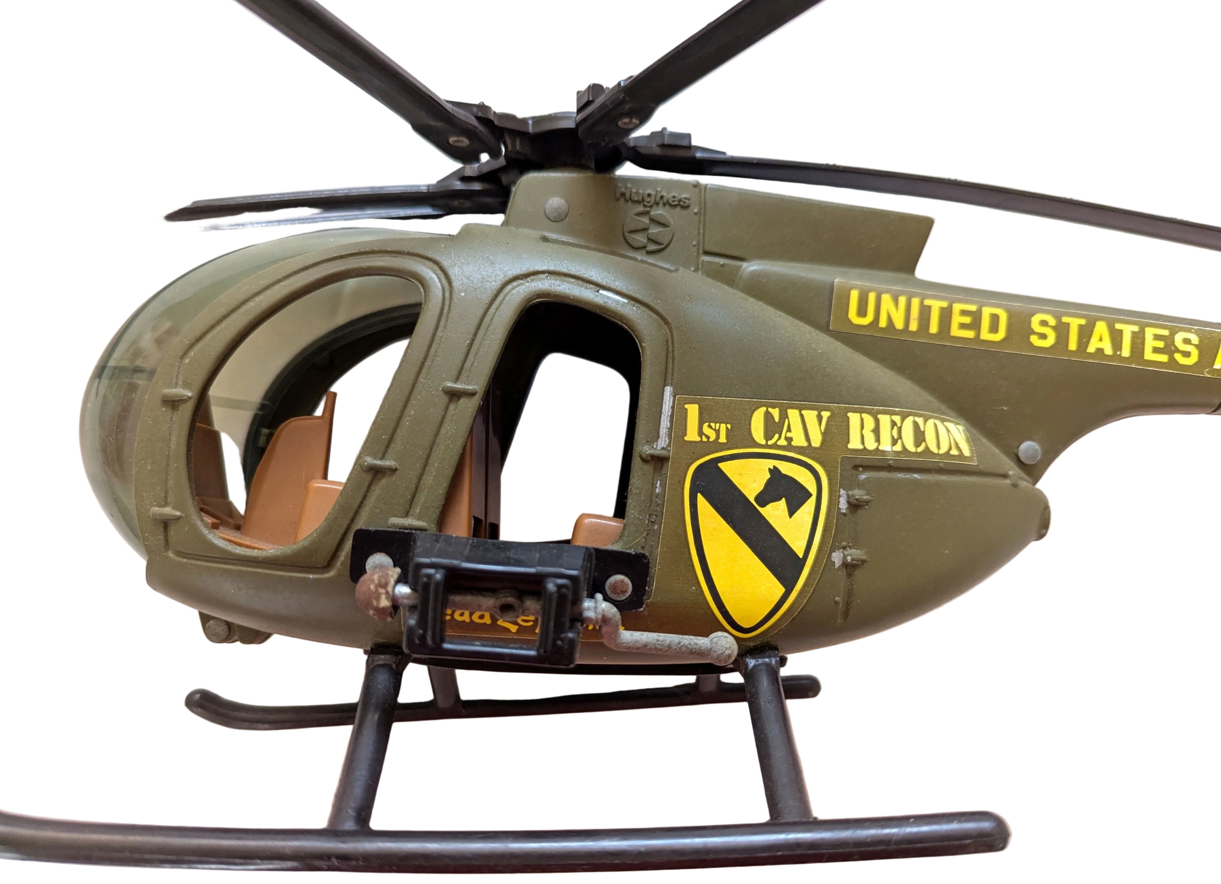 A vintage toy or model military helicopter in olive drab green with yellow and black markings, including 'UNITED STATES' and '1st Cav Recon' with a shield emblem, photographed on a light beige surface.