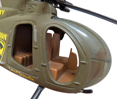 Close-up of a toy helicopter body in olive green with tan seats visible through the open windows and yellow 'Lead Zeppelin' text on the side.