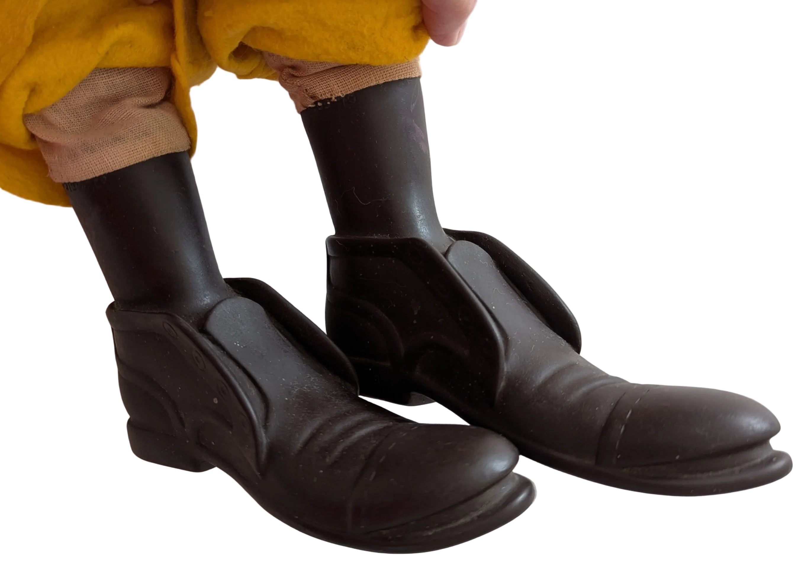A close-up of a doll or toy's legs wearing black slip-on boots and black socks, with a yellow garment at the top, set against a light-colored floor.