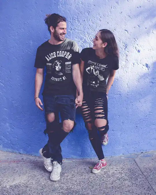 Two people wearing graphic t-shirts against a blue wall.