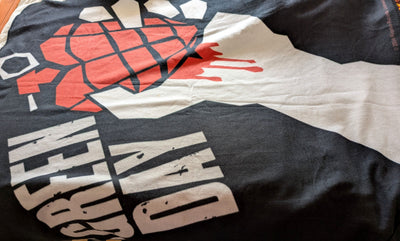 A close-up of a black blanket featuring the iconic Green Day 'Grenade' graphic with a red hand grenade and white text.